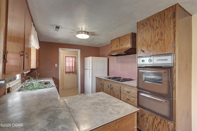 kitchen with wall oven, light countertops, freestanding refrigerator, tasteful backsplash, and stainless steel gas stovetop