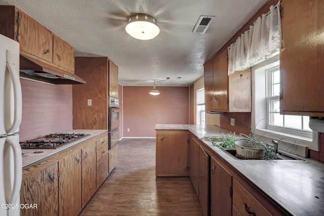 kitchen with wall oven, visible vents, freestanding refrigerator, under cabinet range hood, and stainless steel gas cooktop