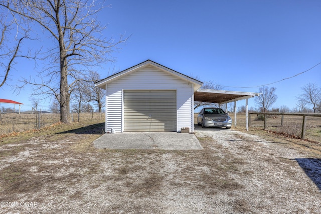 garage featuring driveway, a detached garage, and fence