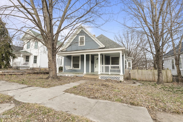 view of front facade featuring a porch, fence, and a shingled roof