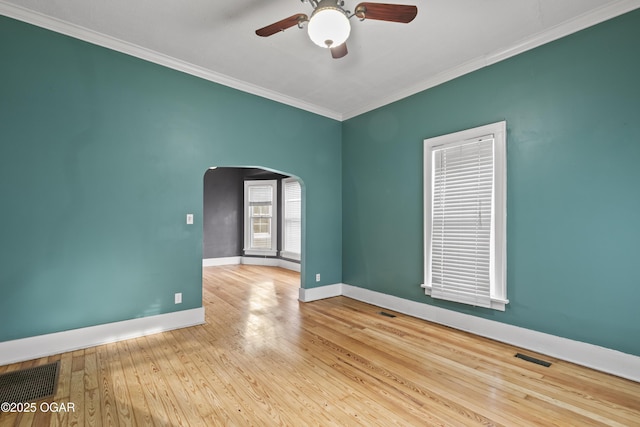 empty room featuring ornamental molding, arched walkways, wood-type flooring, and baseboards