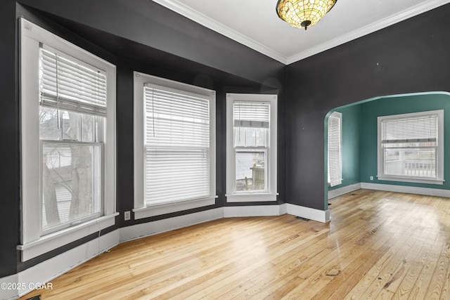 empty room featuring plenty of natural light, wood-type flooring, crown molding, and arched walkways