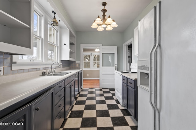 kitchen featuring dark floors, open shelves, light countertops, a sink, and white appliances