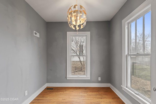 unfurnished dining area with a chandelier, wood finished floors, visible vents, and baseboards