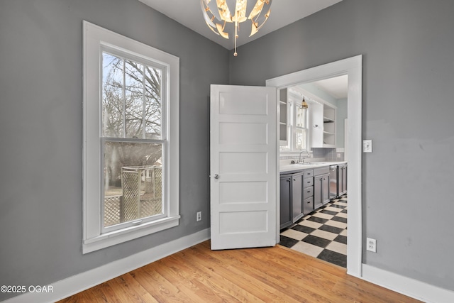 unfurnished dining area featuring a chandelier, baseboards, a sink, and light floors