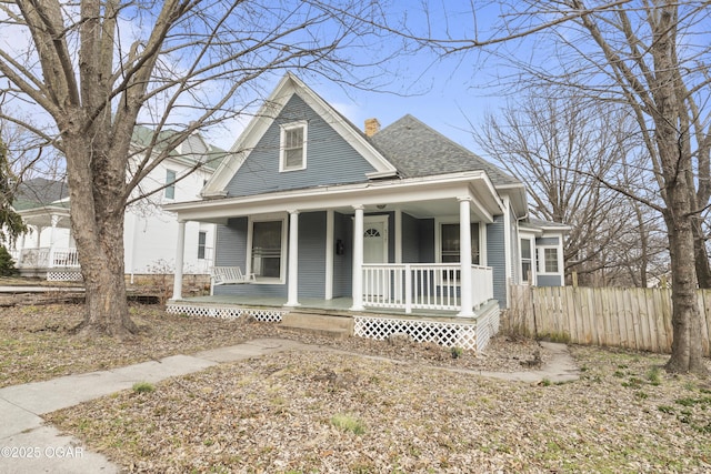 view of front of home with a shingled roof, covered porch, fence, and a chimney