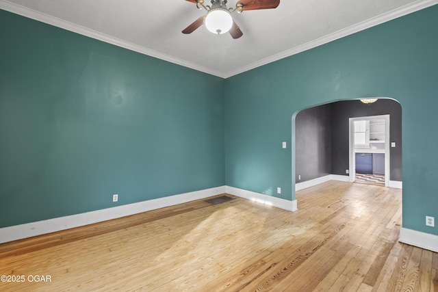 spare room featuring baseboards, arched walkways, a ceiling fan, ornamental molding, and hardwood / wood-style floors