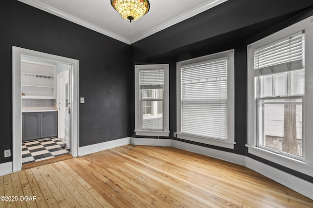 empty room with light wood-style flooring, ornamental molding, and baseboards