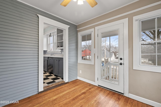 doorway to outside featuring ceiling fan, a sink, baseboards, ornamental molding, and light wood finished floors