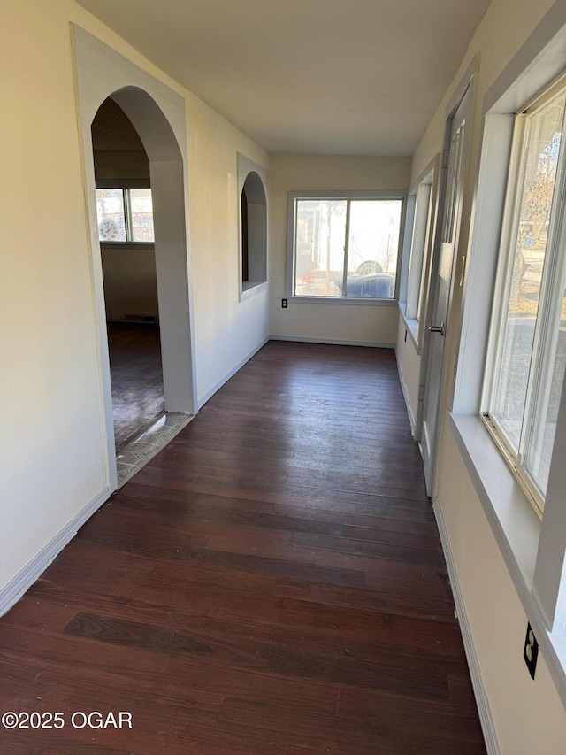 unfurnished room with arched walkways, dark wood-type flooring, and plenty of natural light