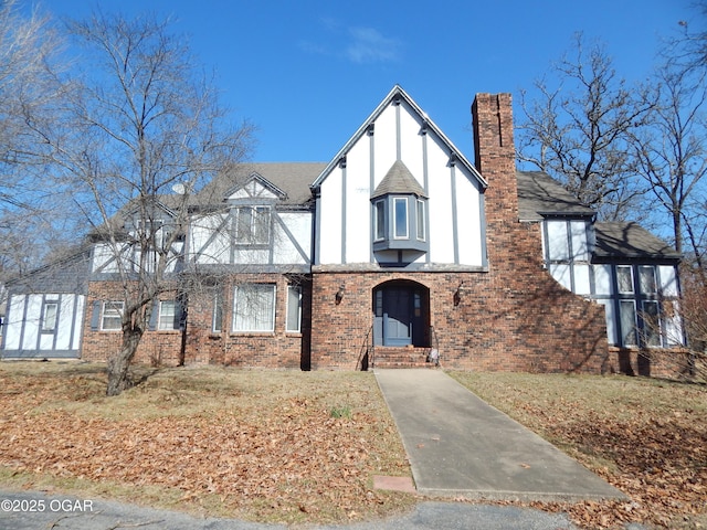 tudor home with roof with shingles, brick siding, a chimney, and stucco siding