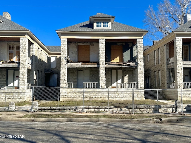 view of front of house featuring roof with shingles, a fenced front yard, and stone siding