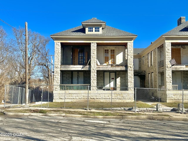 view of front of home featuring stone siding, a fenced front yard, and roof with shingles