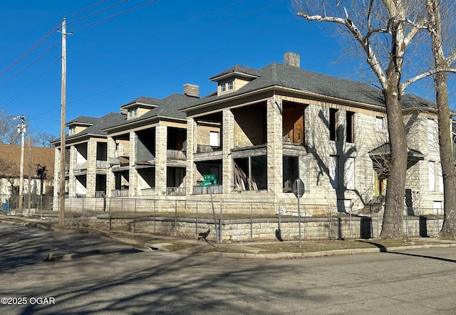 view of front of property featuring a fenced front yard, stone siding, a shingled roof, and a chimney