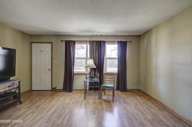 living area with baseboards, light wood-style flooring, and a textured ceiling