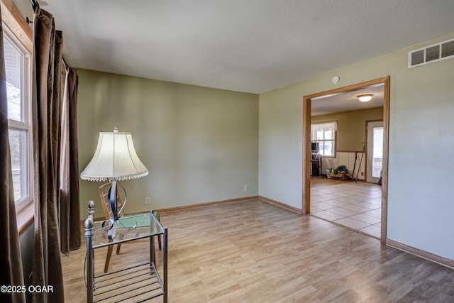 living area featuring light wood-style floors, baseboards, visible vents, and a textured ceiling