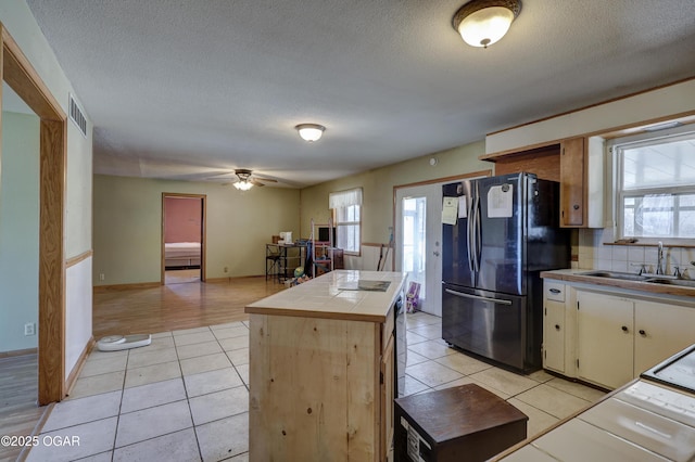 kitchen with tile countertops, light tile patterned floors, a sink, visible vents, and freestanding refrigerator