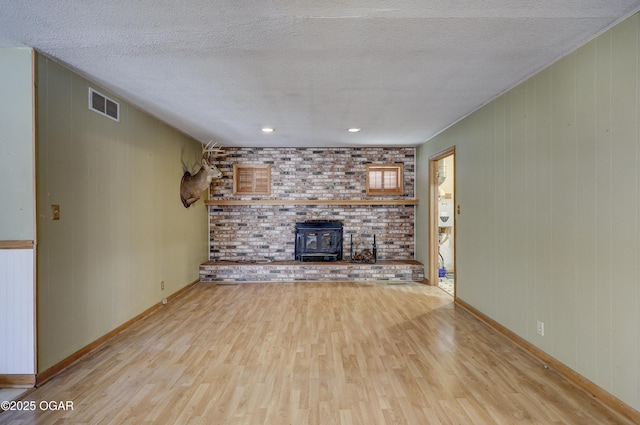 unfurnished living room featuring visible vents, a wood stove, a textured ceiling, wood finished floors, and baseboards