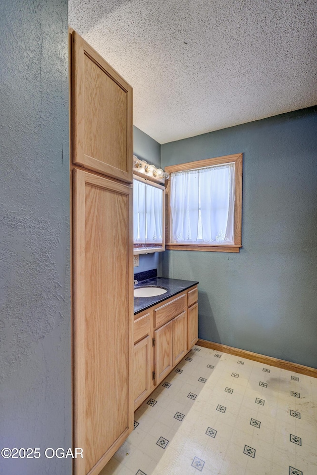 kitchen featuring dark countertops, baseboards, a textured wall, and light floors