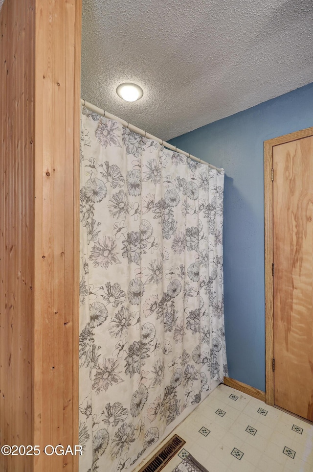 full bath featuring a shower with curtain, baseboards, a textured ceiling, and tile patterned floors