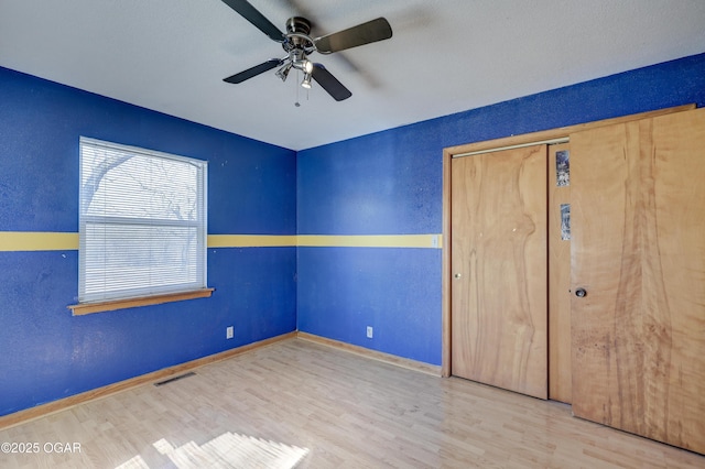 unfurnished bedroom featuring baseboards, visible vents, a ceiling fan, wood finished floors, and a closet