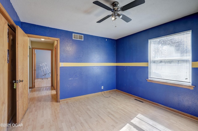 unfurnished room with visible vents, a textured wall, baseboards, and wood finished floors