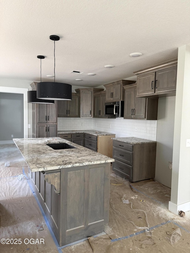 kitchen with light stone countertops, a kitchen island, stainless steel microwave, and backsplash