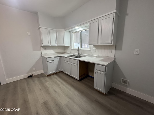 kitchen with light countertops, a sink, baseboards, and wood finished floors