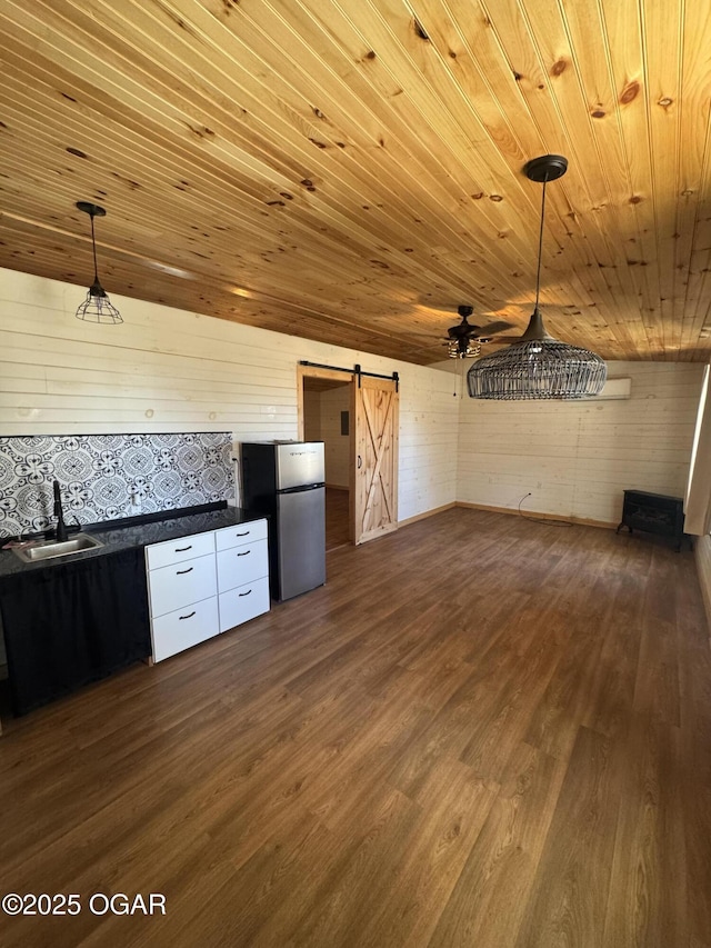 kitchen with a barn door, dark wood-style flooring, a sink, freestanding refrigerator, and dark countertops