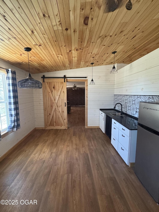 kitchen with a barn door, dark wood finished floors, dark countertops, wooden ceiling, and freestanding refrigerator