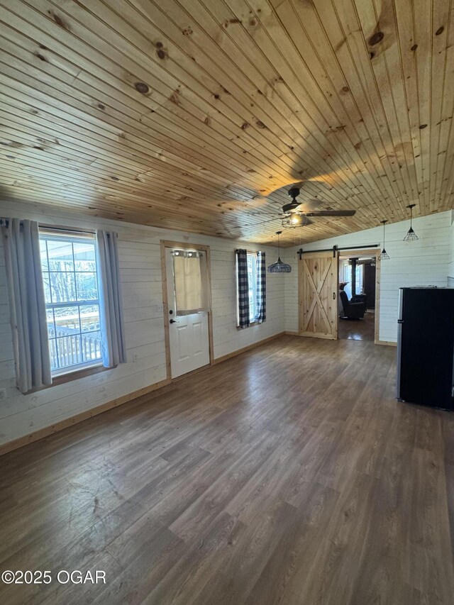 unfurnished living room with wooden ceiling, a barn door, dark wood finished floors, and a ceiling fan