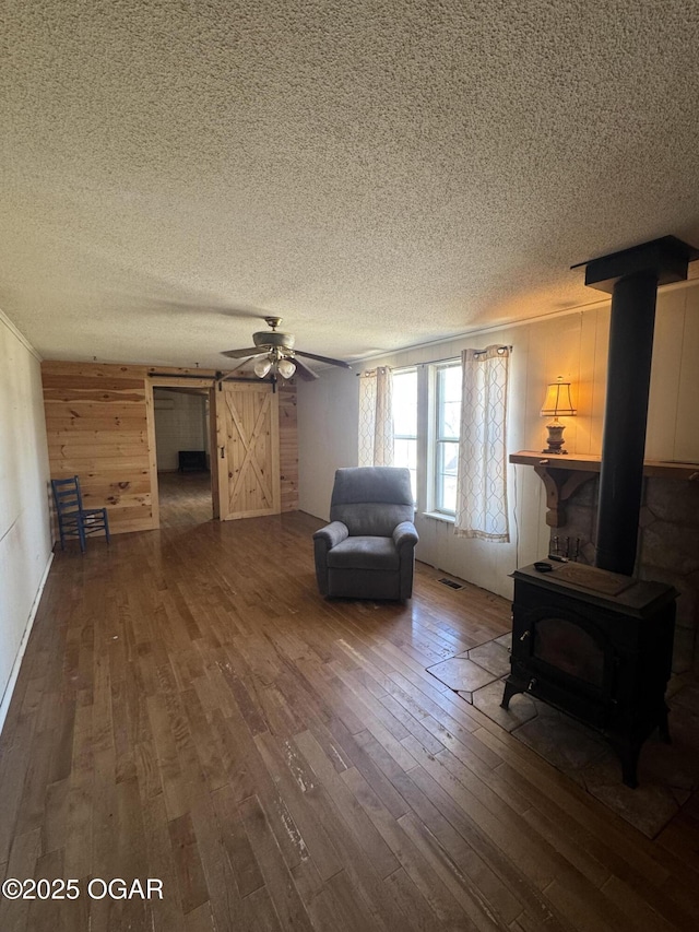 unfurnished living room with a wood stove, visible vents, wood-type flooring, and a textured ceiling