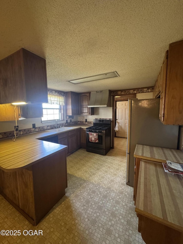 kitchen featuring light floors, stainless steel appliances, a sink, a peninsula, and wall chimney exhaust hood