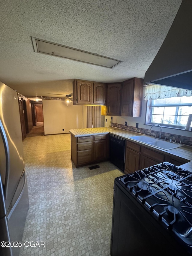 kitchen with a peninsula, a sink, visible vents, range hood, and black appliances