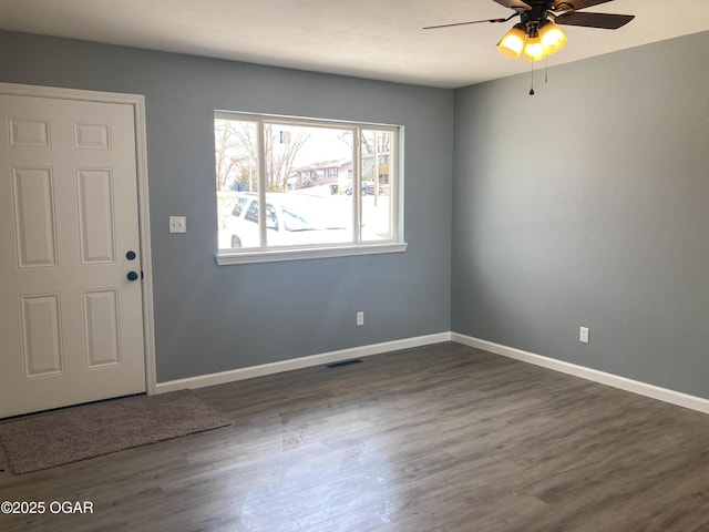 unfurnished room with dark wood-style floors, visible vents, baseboards, and a ceiling fan