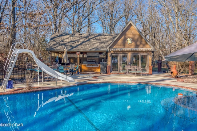 outdoor pool with fence, a water slide, an outdoor structure, a patio area, and an exterior structure