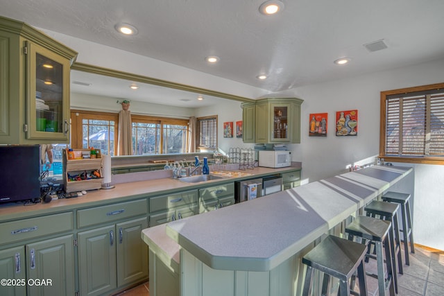 kitchen with green cabinets, white microwave, a breakfast bar area, and recessed lighting