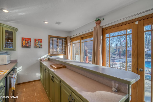 kitchen with green cabinets, white microwave, a wealth of natural light, and visible vents