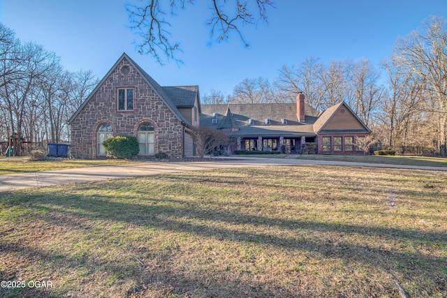 view of front of house featuring driveway, stone siding, a chimney, and a front lawn