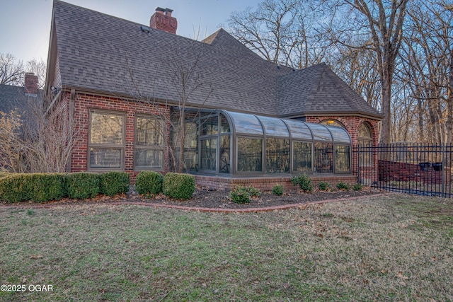 back of house with brick siding, a shingled roof, fence, a sunroom, and a chimney