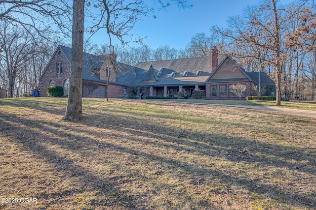 view of front of property featuring brick siding, a chimney, and a front yard