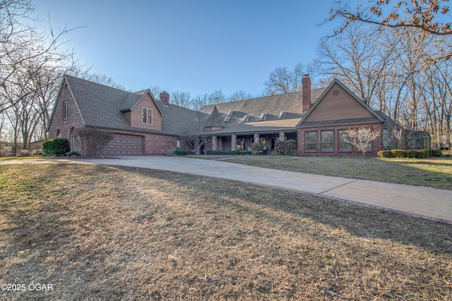 view of front facade with brick siding, a chimney, concrete driveway, an attached garage, and a front lawn