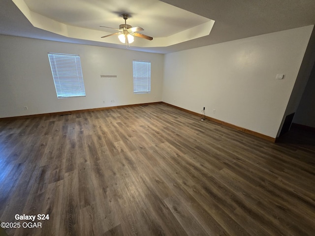 interior space featuring a ceiling fan, dark wood-style flooring, a raised ceiling, and baseboards