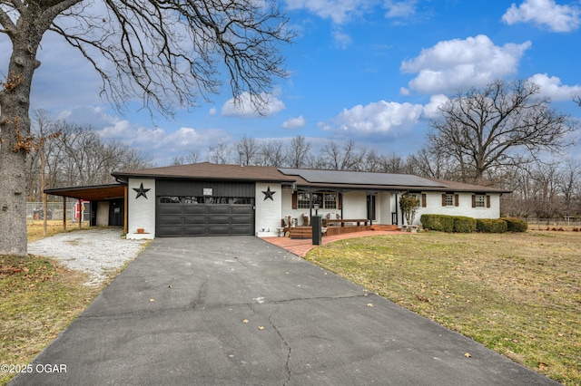 view of front of house with aphalt driveway, an attached garage, covered porch, solar panels, and a front yard