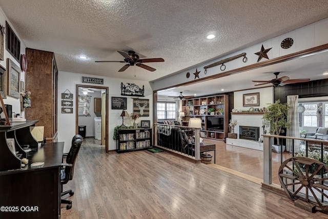 office area featuring wood finished floors, a wealth of natural light, a fireplace, a ceiling fan, and a textured ceiling