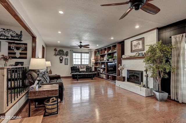 living area with a textured ceiling, ceiling fan, recessed lighting, a brick fireplace, and wood finished floors