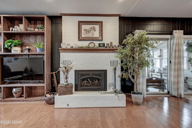 living area with a textured ceiling, wood finished floors, and a brick fireplace