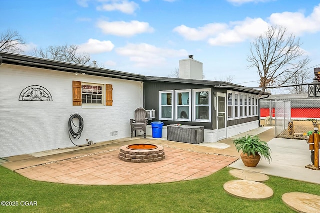 rear view of house featuring a fire pit, a patio, a chimney, fence, and a sunroom