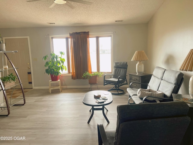 living room featuring light wood-style floors, visible vents, a textured ceiling, and baseboards