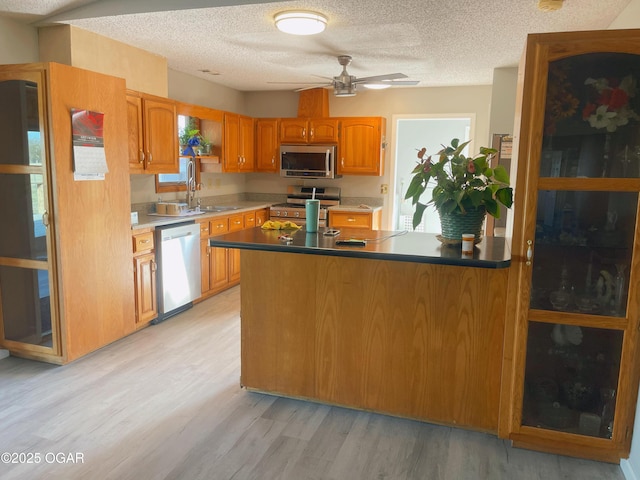 kitchen with stainless steel appliances, a sink, a textured ceiling, light wood-type flooring, and a peninsula